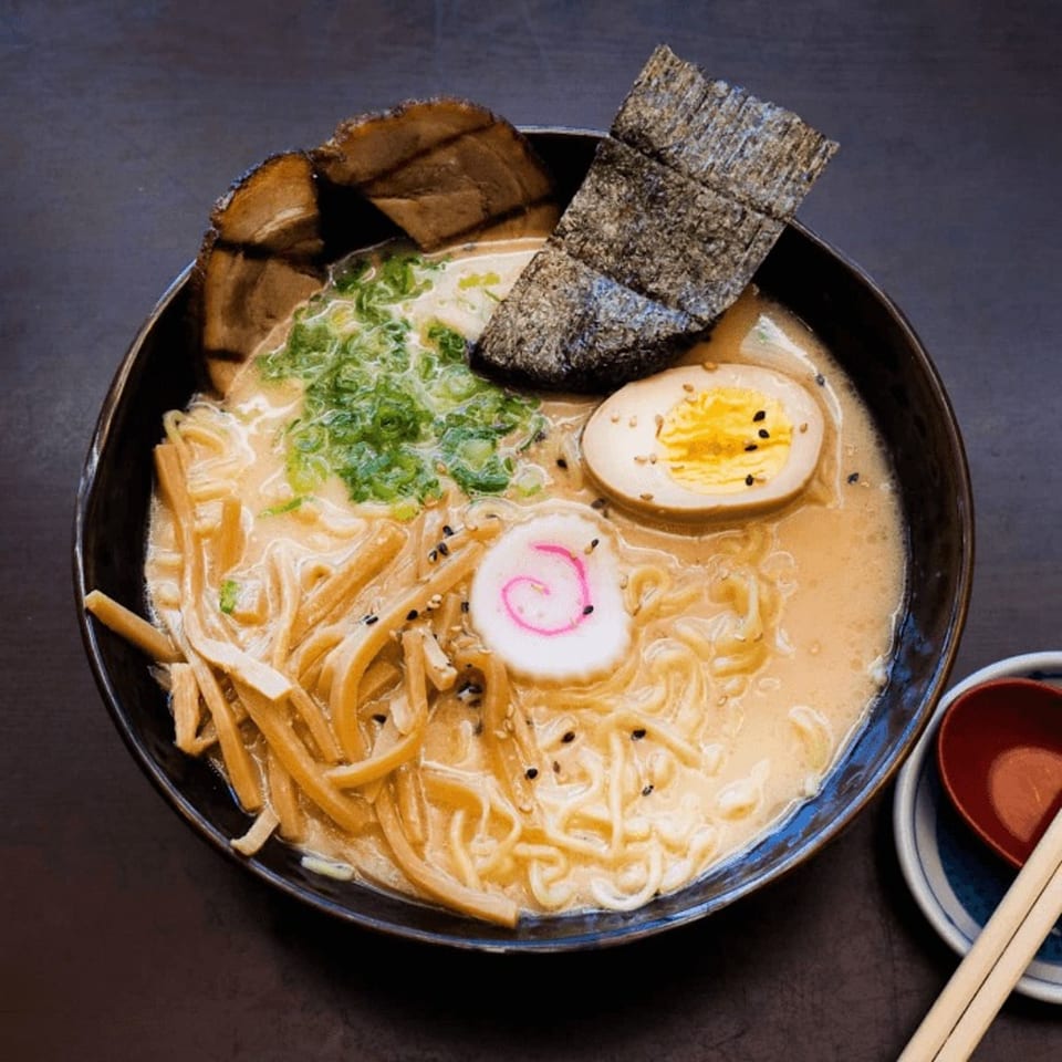 A bowl of ramen with pork, seaweed, egg, green onions, and a pink swirled fish cake.