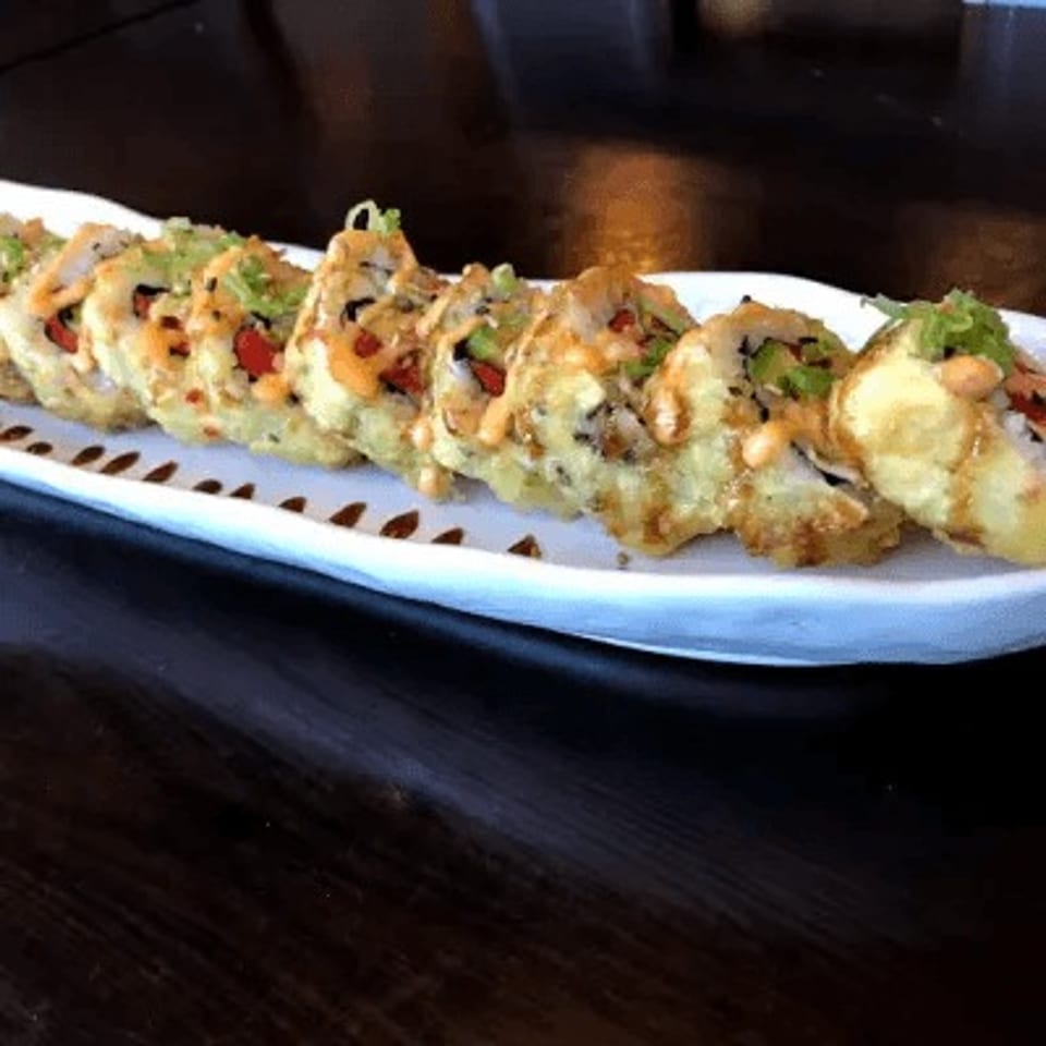 Tempura-fried sushi rolls with spicy sauce and green onions on a white rectangular plate.